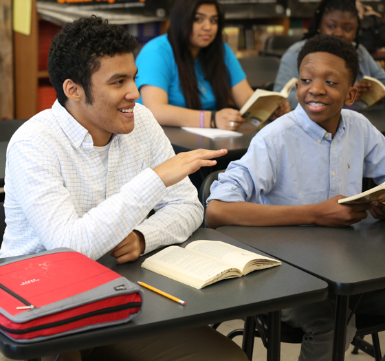 students smiling while discussing a book in class