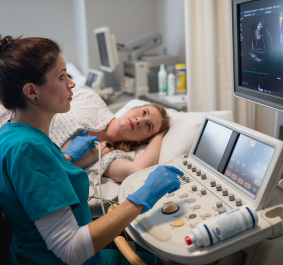 non-invasive cardiovascular technology student testing ultrasound equipment on patient, looking at results on screen