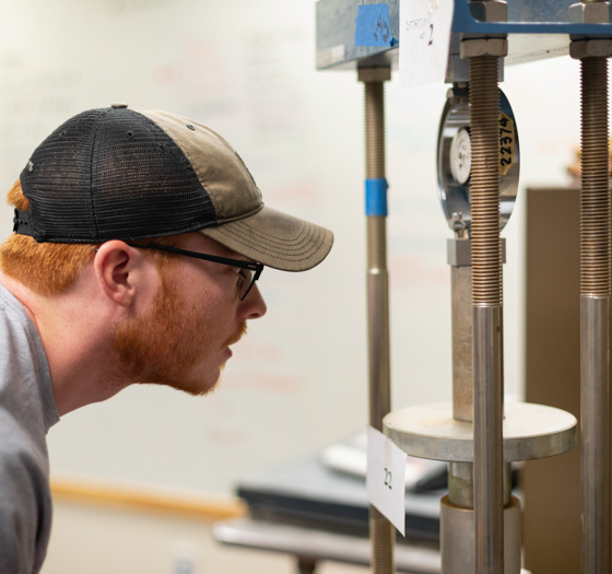 civil engineering student wearing hat examining some pipes and a meter