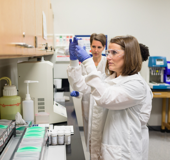 cytotechnology student wearing lab coat, gloves, and goggles examining a specimen