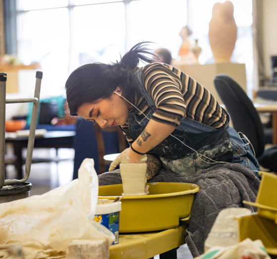 a student in overalls working at a pottery wheel