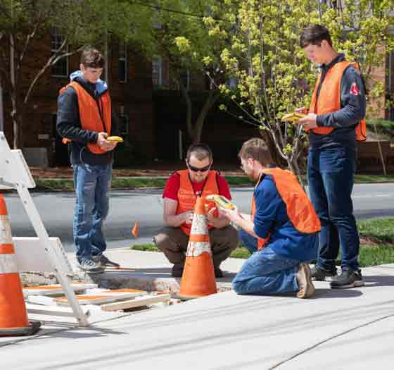 four students in vests learning Geomatics Technology surveying sidewalk