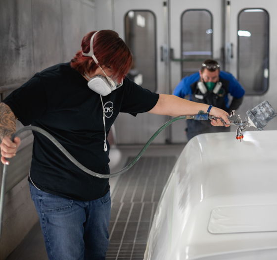 collision repair and refinishing technology student wearing protective equipment spraying paint on a car