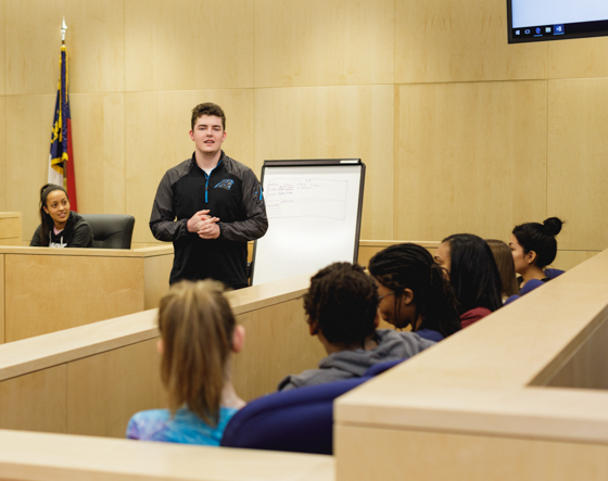 students demonstrating a case in a court room - one student in judge seat, 6 students in jury, and one student presenting evidence