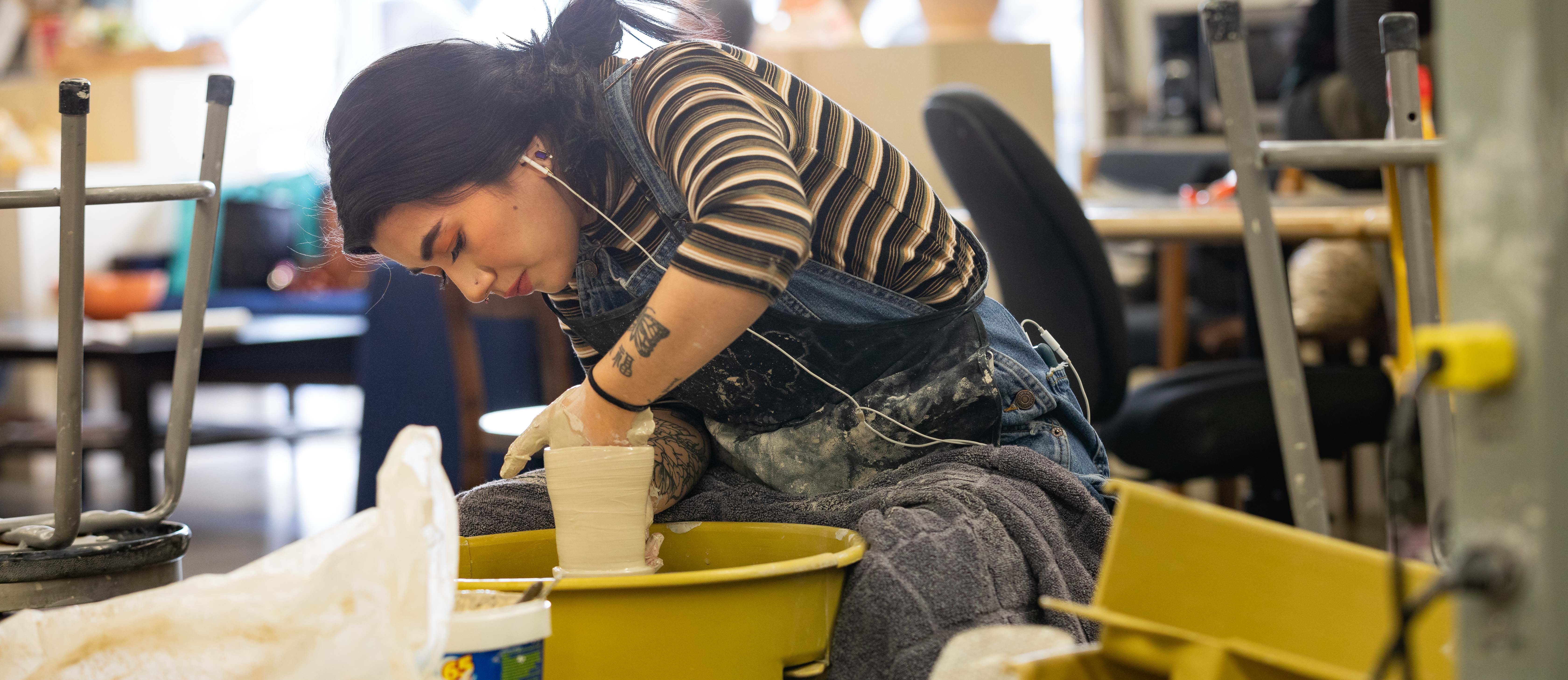 a student in overalls working at a pottery wheel