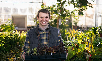 Christopher Breedlove standing in a greenhouse with plants in his hand