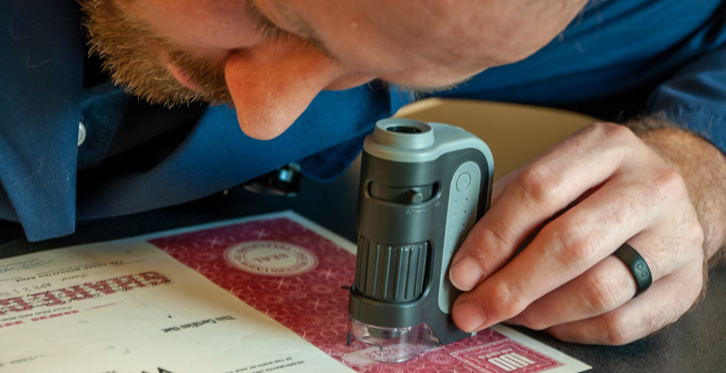 man leaning over document using magnifying tool to check authenticity