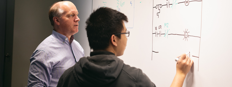 a student doing a complicated problem on a board with his instructor