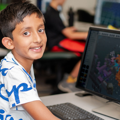 young student smiling at a computer as he learns to code