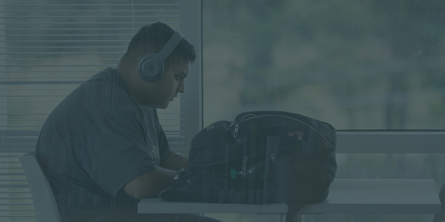male student working at a desk with headphones on