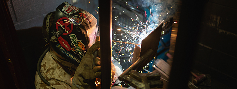 student in welding mask making sparks as he welds