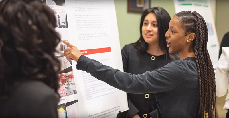 three female students interacting with an engineering presentation board