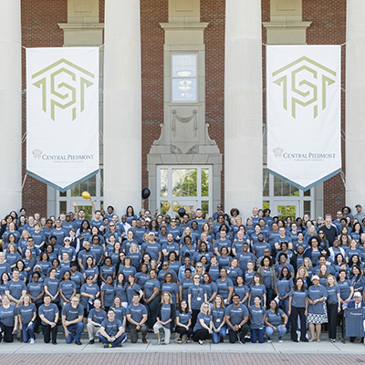 big group of Central Piedmont employees wearing Central Piedmont tshirts standing on steps of Overcash Center with Central Piedmont logo banners