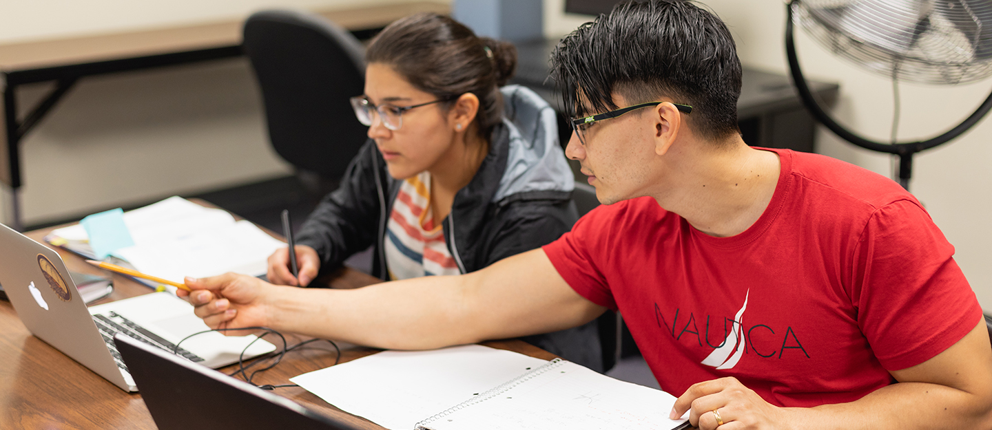 tutor helping student at table at tutoring center pointing at laptop