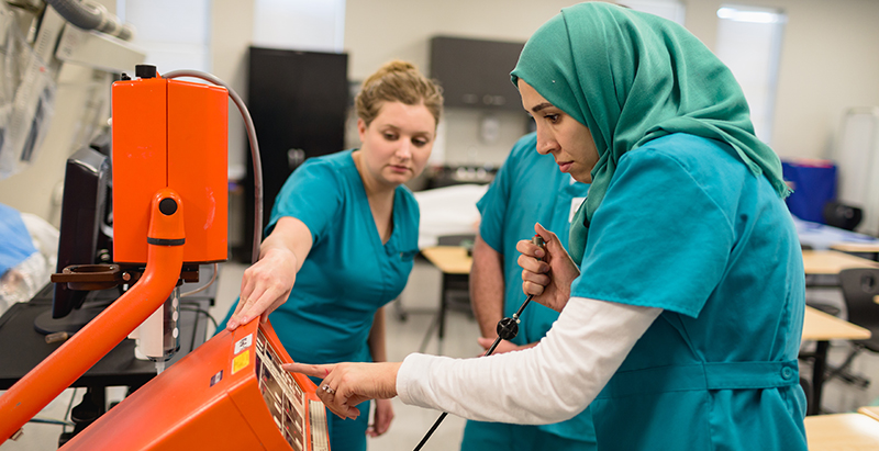 healthcare students in scrubs learning how to use a machine