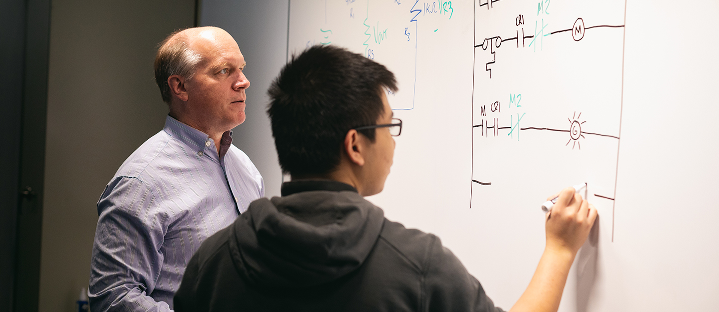 a student doing a complicated problem on a board with his instructor