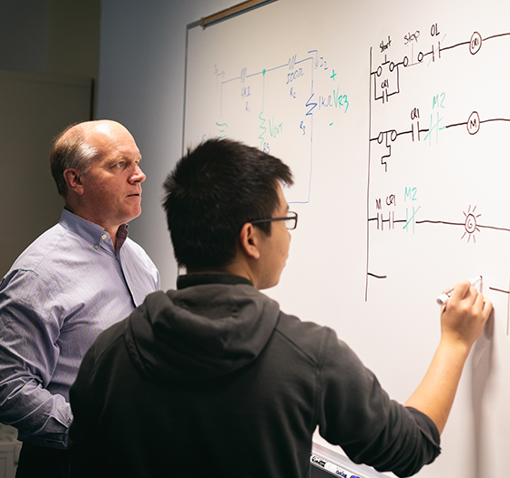 a student doing a complicated problem on a board with his instructor