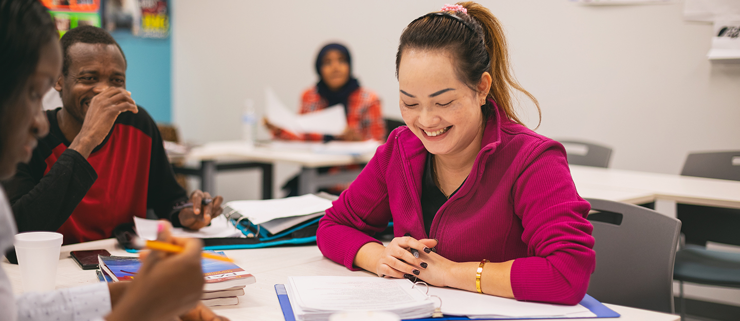 ESL students smiling as they work on coursework together in classroom