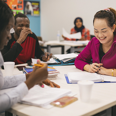 ESL students smiling as they work on coursework together in classroom