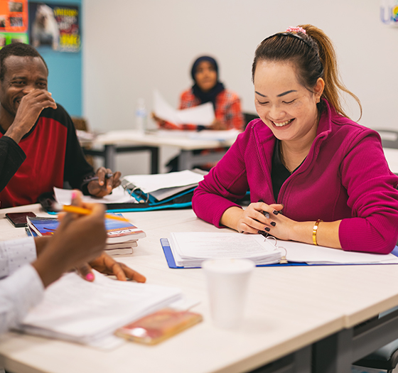 ESL students smiling as they work on coursework together in classroom