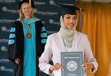 Class of 2020 graduate wearing graduation cap and tassel and holding commencement program in front of Dr. Deitemeyer at graduation ceremony