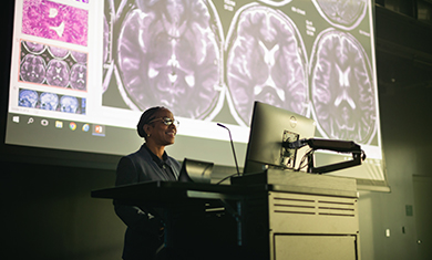 instructor at podium in front of screen showing slides of the human brain