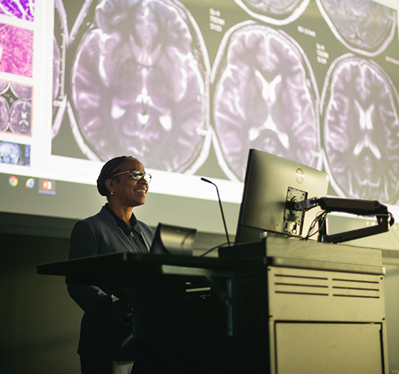 instructor at podium in front of screen showing slides of the human brain