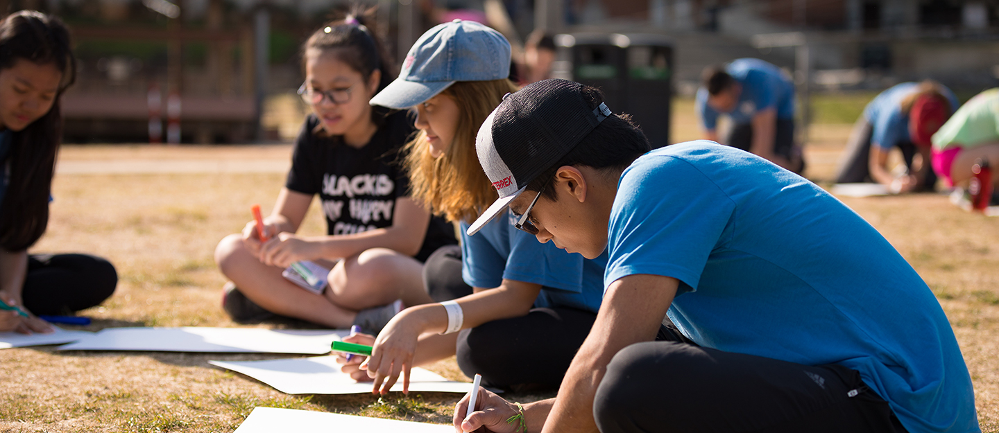 students sitting in grass outside collaborating on a project