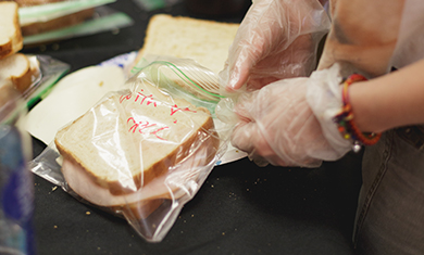 a volunteer wearing gloves putting a freshly prepared sandwich into a sandwich bag