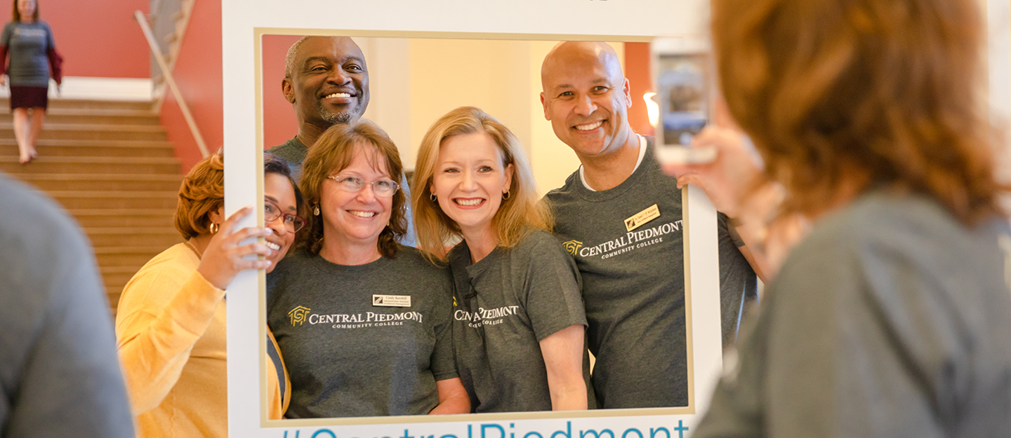 Central Piedmont president Dr. Deitemeyer and employees in group photo with cardboard Instagram post frame