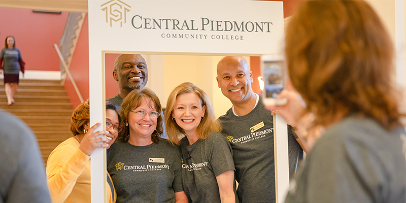 Central Piedmont president Dr. Deitemeyer and employees in group photo with cardboard Instagram post frame