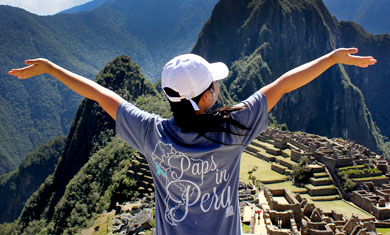 student in hat looking over Machu Picchu, Peru with arms out