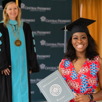 a student in their graduation cap holding their diploma in front of CPCC President Dr. Kandi Deitemeyer at the 2020 Central Piedmont graduation ceremony