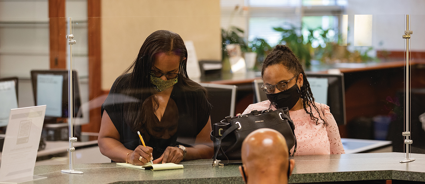 a student and their mother, wearing masks, filling out paperwork at a Central Piedmont service desk