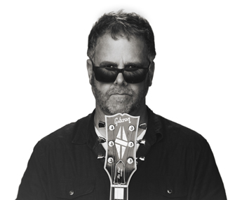 Chris Brawley portrait, wearing sunglasses and resting chin on guitar