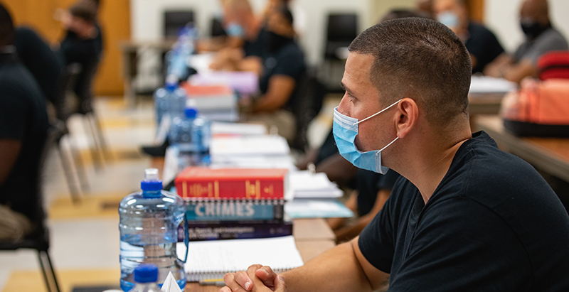 student wearing mask listening in class with stack of textbooks