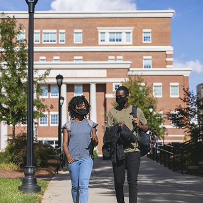 two students wearing masks chatting while walking on Central Campus