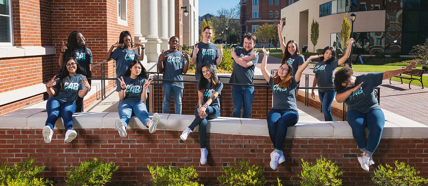 Campus Activities Board members sitting on railing in front of North Campus Building making silly poses