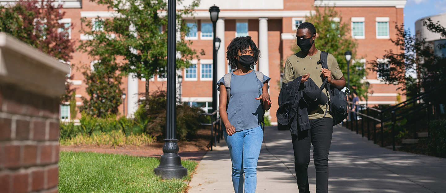 two students wearing masks and walking outside at the Central Campus quad