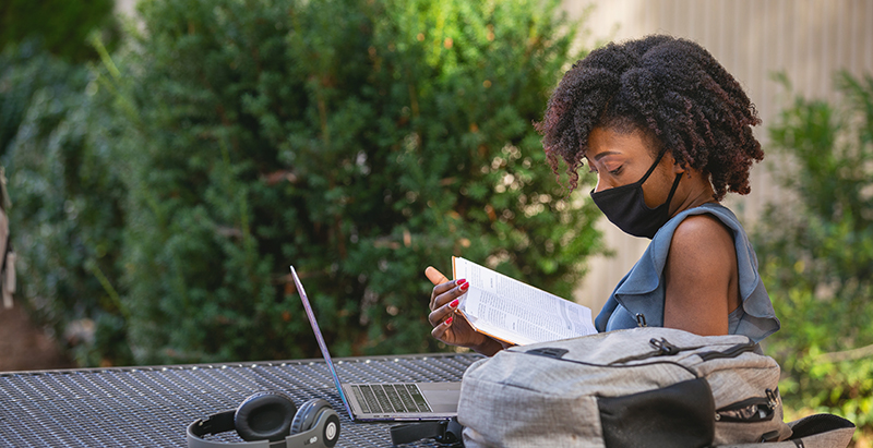 student wearing mask studying book at outside table