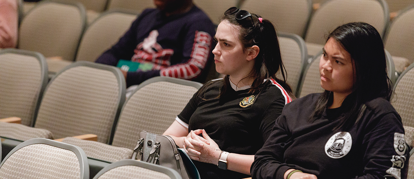 students sitting in an auditorium listening to a panel discussion