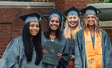 2021 graduates smiling outside in caps and gowns holding up commencement programs