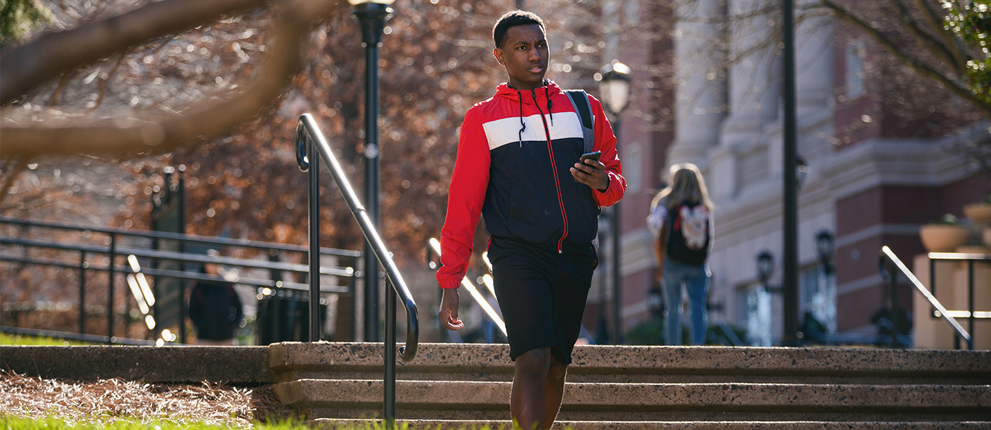 student walking outside carrying backpack through campus