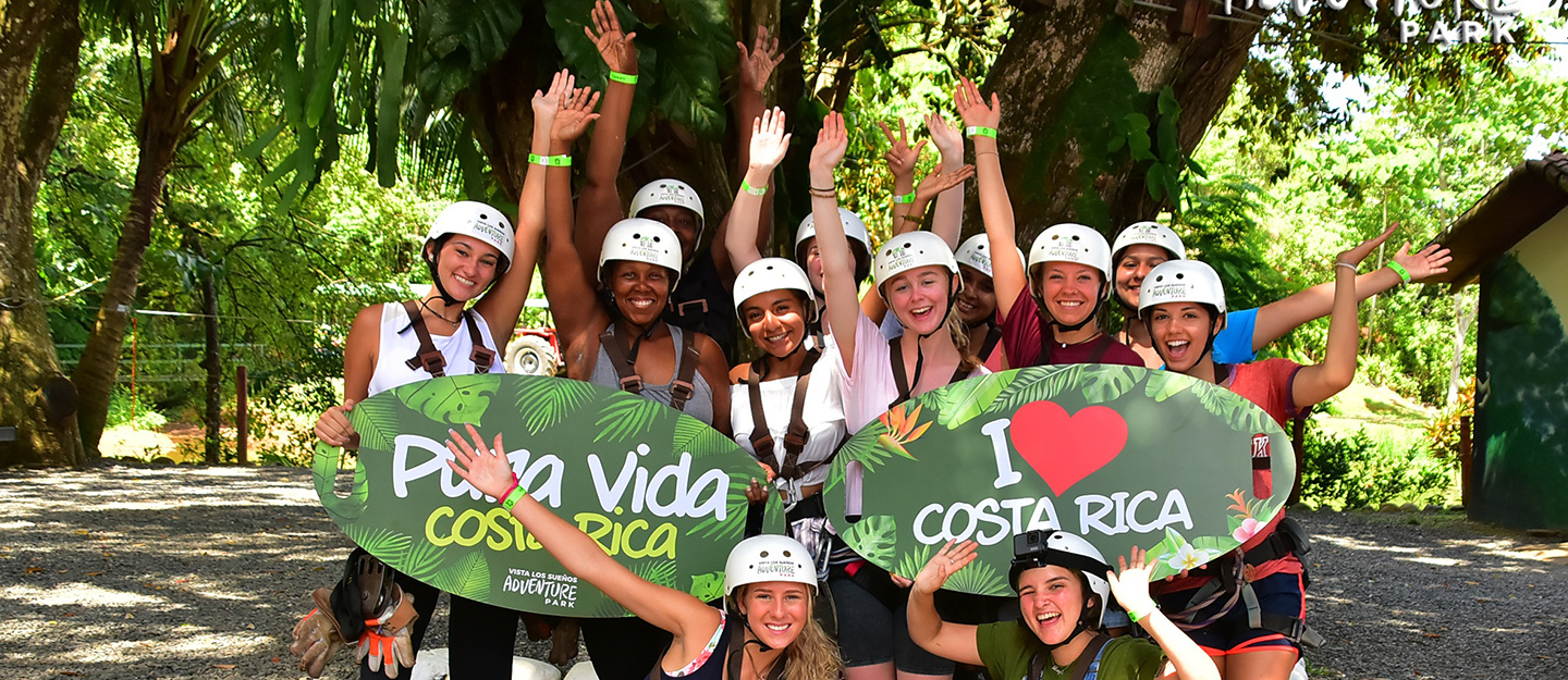 Costa Rica study abroad students doing excited pose in jungle, holding signs that say Pura Vida and I love Costa Rica