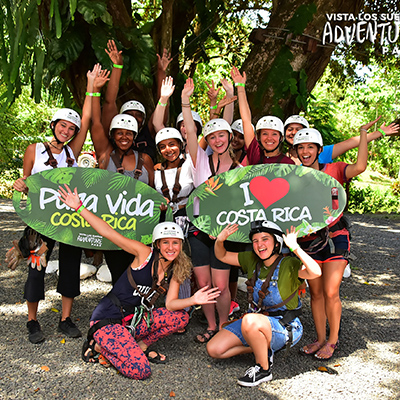 Costa Rica study abroad students doing excited pose in jungle, holding signs that say Pura Vida and I love Costa Rica