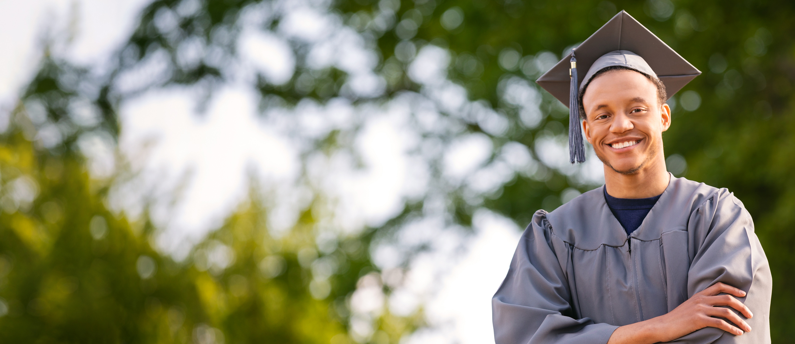 diverse student wearing cap and gown outside at graduation