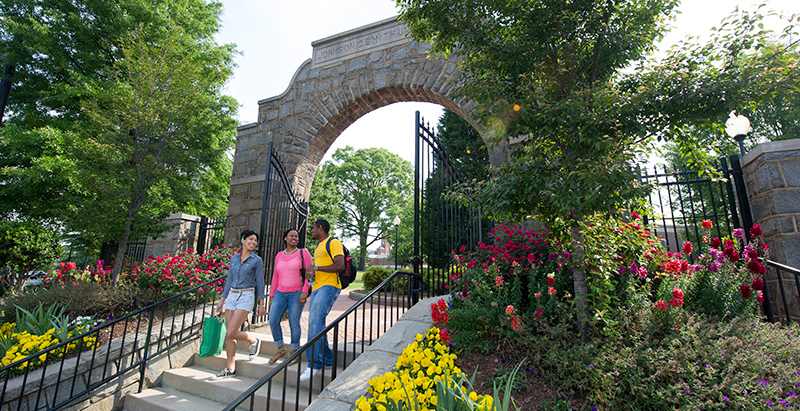 three diverse students walking and talking on steps under a stone archway on Johnson C. Smith campus