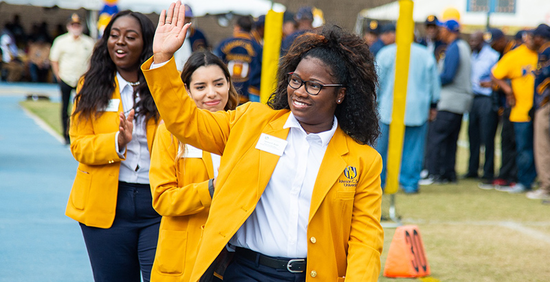 Johnson C. Smith students in college jackets waving as they walk across a stage