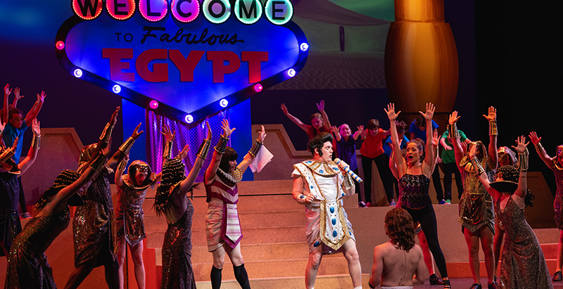 Egyptian pharaoh from joseph and the amazing technicolor dreamcoat singling with chorus, "Welcome to Fabulous Egypt" sign (like Las Vegas sign) in background