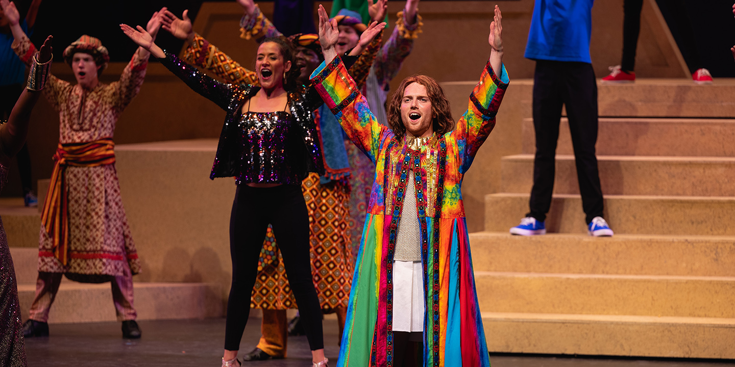 cast/chorus of Joseph and the technical dreamcoat in triumphant poses arms raised with confetti coming down